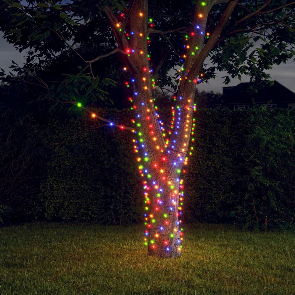 Two strands of colorful solar fairy lights wrapped around a tree trunk at dusk.