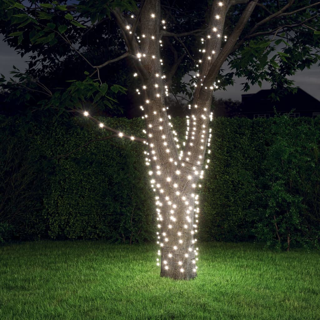A tree in a backyard wrapped with strands of cold white solar fairy lights glowing at night.