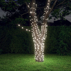 A tree in a backyard wrapped with strands of cold white solar fairy lights glowing at night.