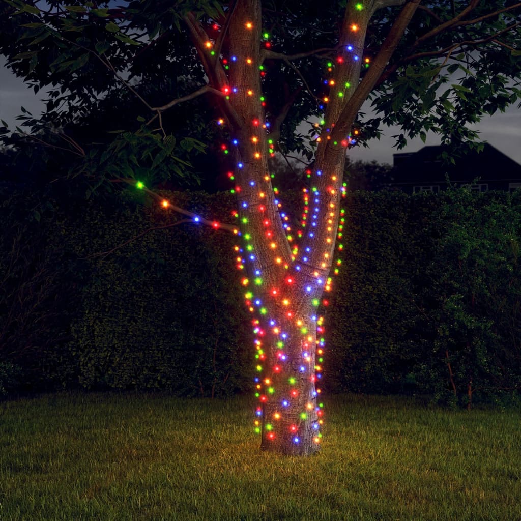 A tree wrapped in colorful solar fairy lights glowing at night in a yard.