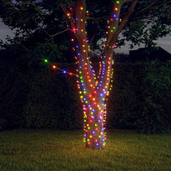 A tree wrapped in colorful solar fairy lights glowing at night in a yard.