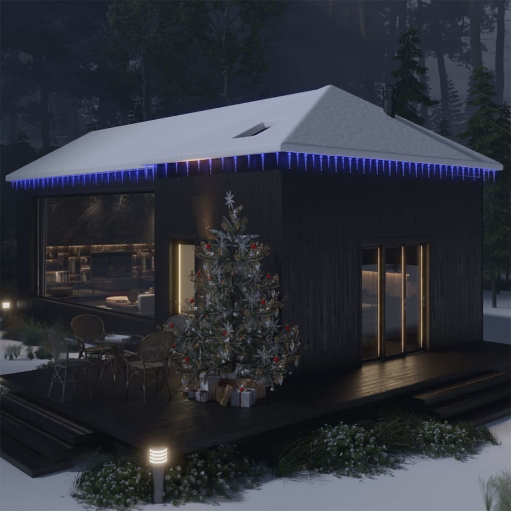 Blue acrylic Christmas icicle lights illuminate the eaves of a snow-covered house.