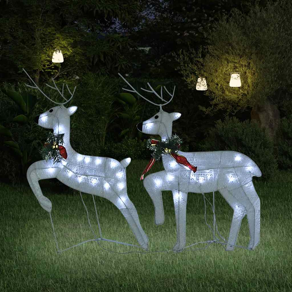 Two white LED-lit reindeer silhouettes with red bows, standing on grass at night.