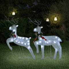 Two white LED-lit reindeer silhouettes with red bows, standing on grass at night.