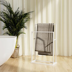 White freestanding iron towel rack with two tiers holding a gray towel in a bathroom.