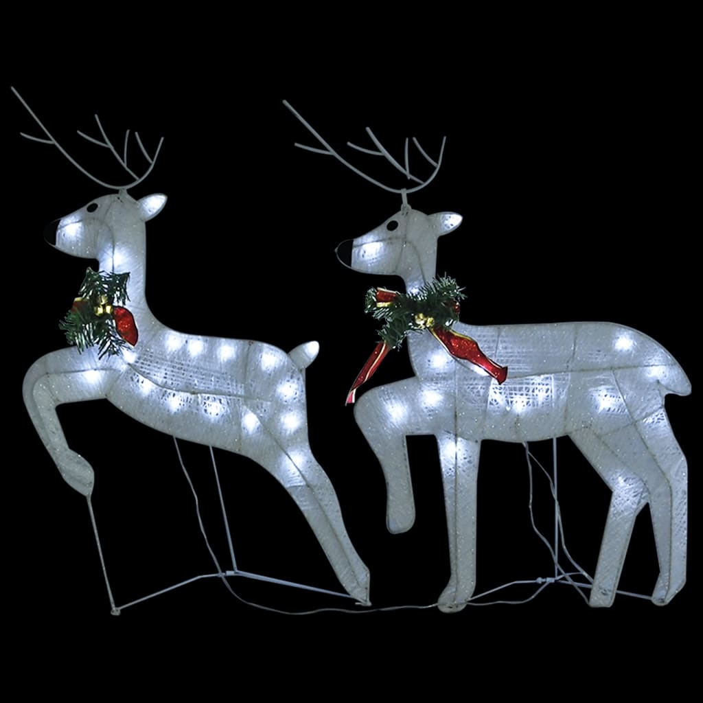 Two white LED-lit reindeer with red bows and holly stand near a sleigh for outdoor Christmas display.