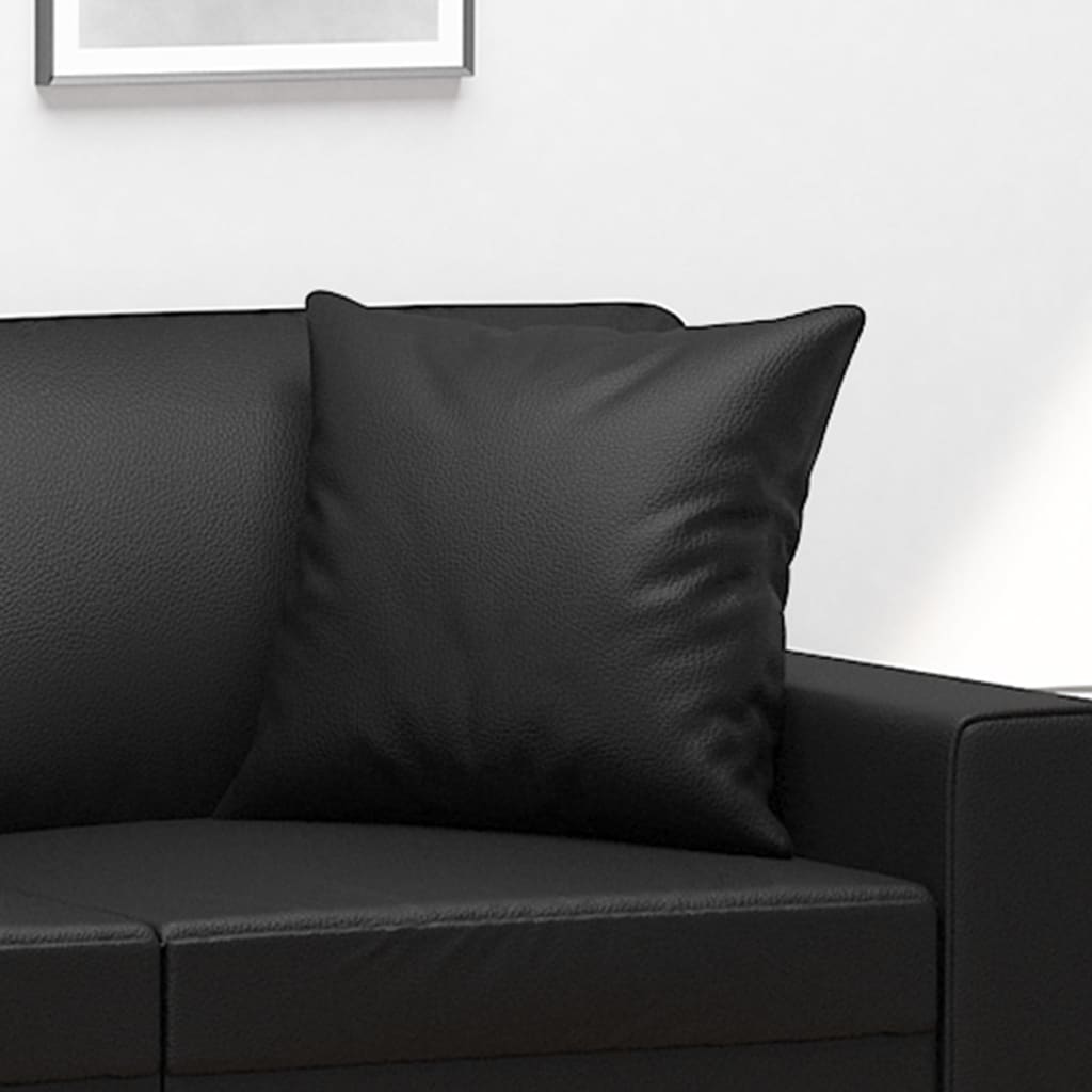 Two black faux leather throw pillows on a black leather sofa.