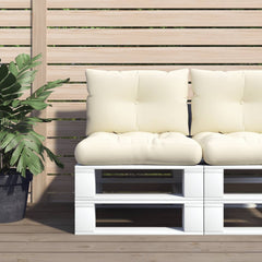 Two cream polyester cushions on a white pallet sofa against a wooden fence with plants.