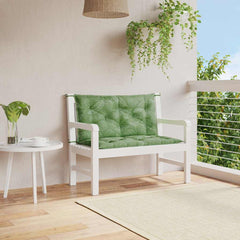 Two green leaf-patterned bench cushions on a white wooden bench in a sunny outdoor patio setting.