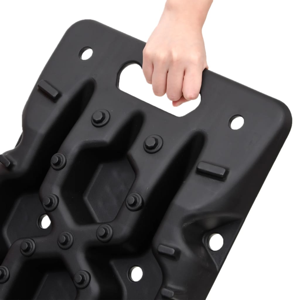 A hand grips the handle of a black nylon traction board with a honeycomb tread pattern.