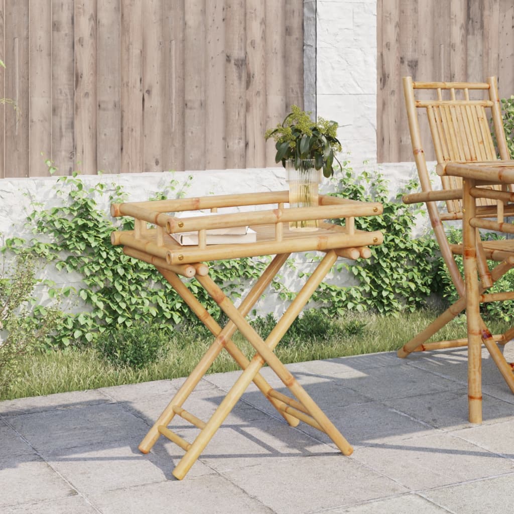 Bamboo folding tray table with book and vase on slatted top, folded legs, outdoors.