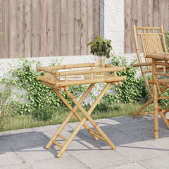 Bamboo folding tray table with book and vase on slatted top, folded legs, outdoors.