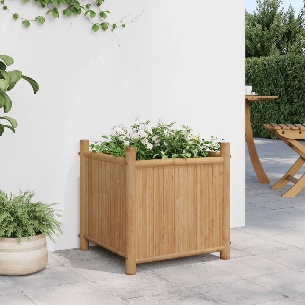 A 15.7-inch square bamboo planter box with white flowers, elevated on a patio.