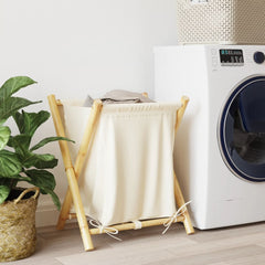 Cream white bamboo laundry basket with fabric liner, folded frame, next to a white washer.