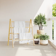 Bamboo double towel ladder with 4 rungs, holding white towels, beside plants.