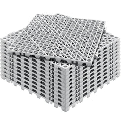Stack of gray PVC interlocking drainage floor mats with a grid pattern and support pins.