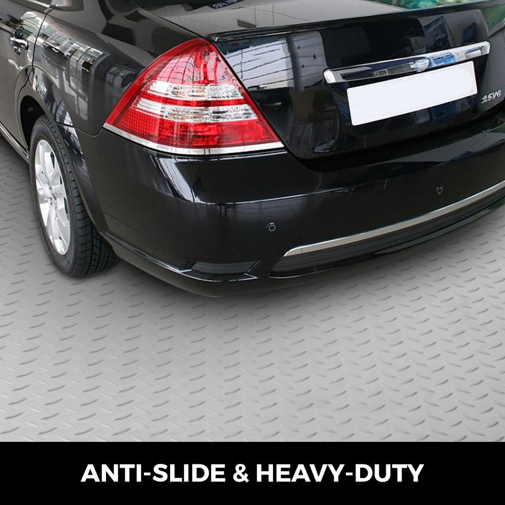 Silver PVC garage floor mat rolled out under a black car's rear tires on a showroom floor.