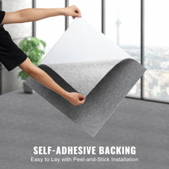 Person holding a 24x24 inch light gray peel-and-stick carpet tile, showing self-adhesive backing.